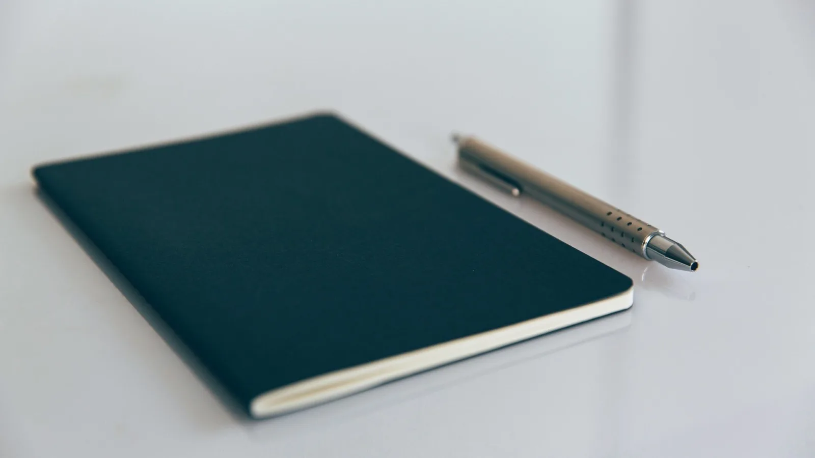 A closed notebook and a pen lying on a desk.